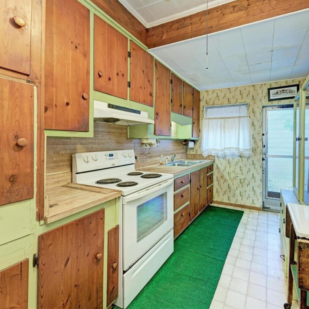 Throwback Kitchen with Vintage Charm Vintage kitchen with green carpeting, wood cabinets with green trim, white electric stove, and dated wallpaper, showing signs of age and wear.