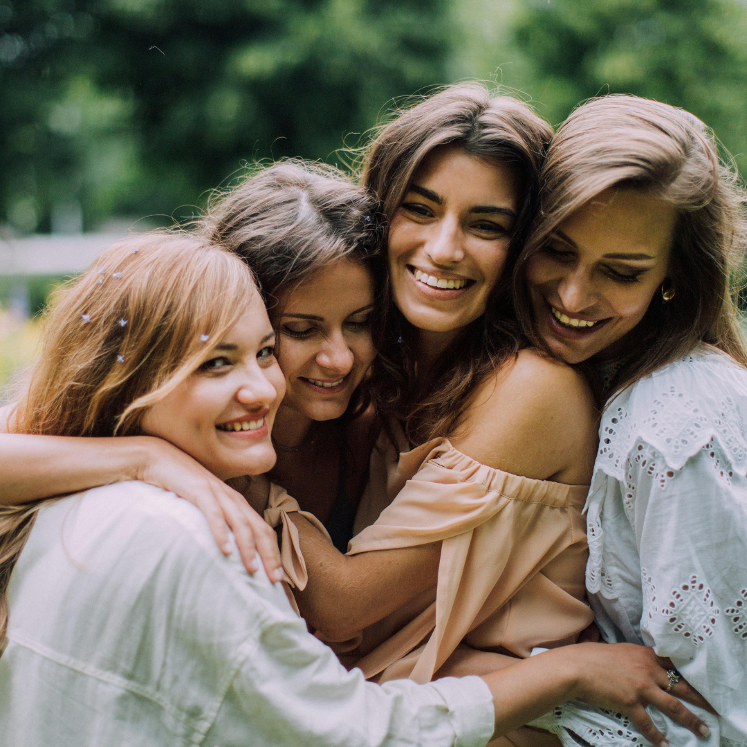 A Peaceful Path Forward - Sell Your House for Cash wit American Hero Properties Four smiling women embracing outdoors, showing closeness and happiness in a peaceful, natural setting.