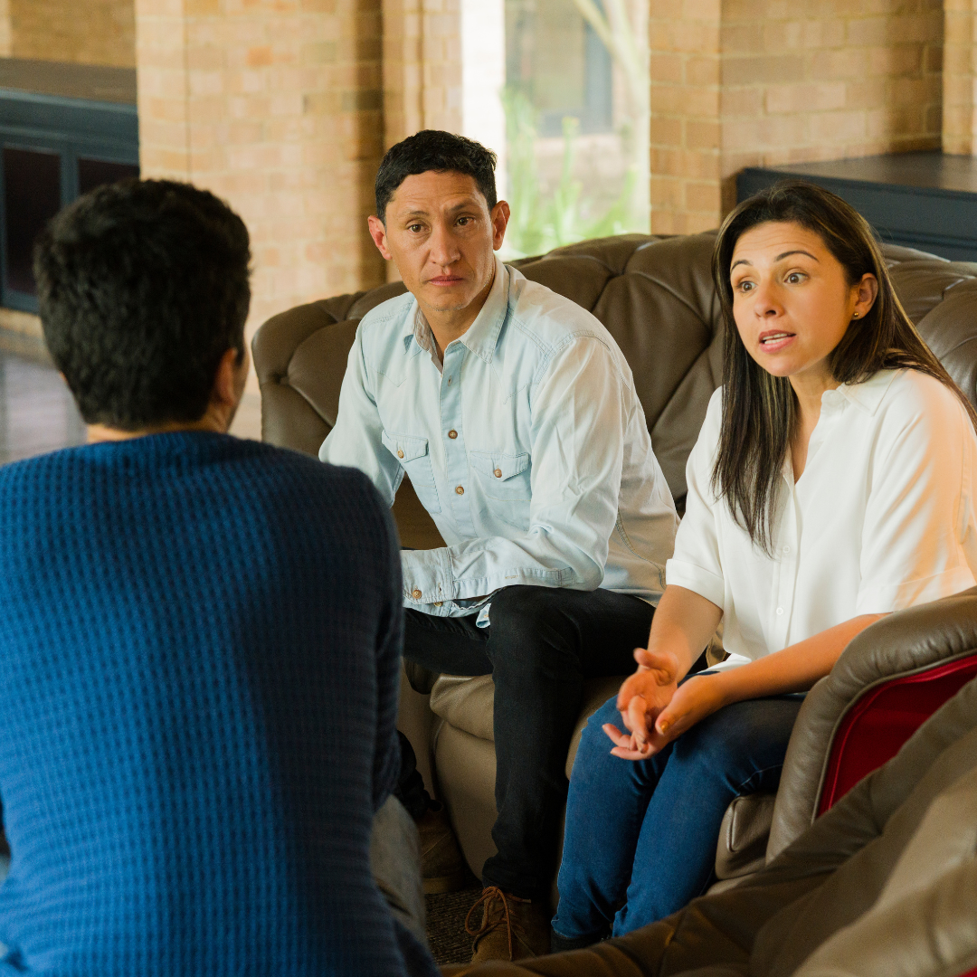 When Everyone Has a Say: Selling with Multiple Heirs Three adults having a serious discussion in a living room, suggesting a family conversation about a shared decision related to selling an inherited property.