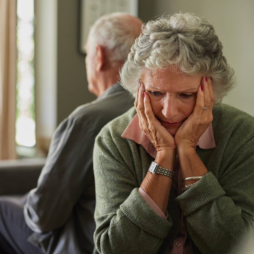 Emotional Strain of Inheriting a Home in Tampa, FL Elderly woman looking distressed with hands on her face, sitting beside an older man turned away, suggesting emotional strain.