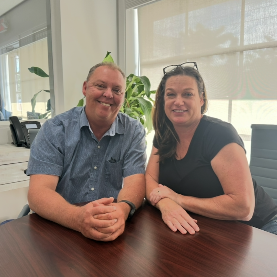 Smiling man and woman seated together at a desk, suggesting a positive and collaborative experience possibly after completing a shared home sale.